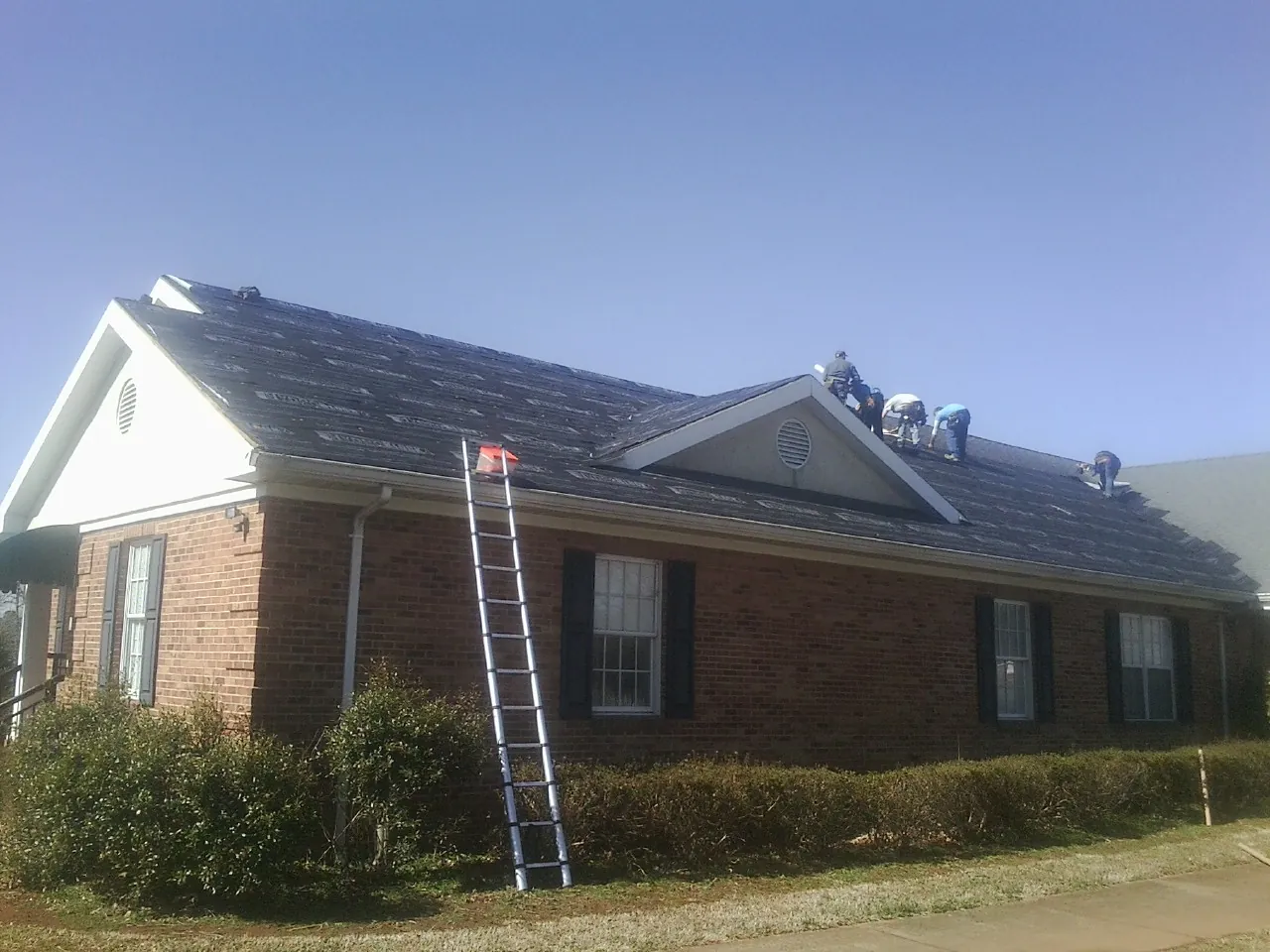 Crew tearing shingles off a brick ranch roof with a ladder set — Metal Roof Repair work by our crew in Napavine