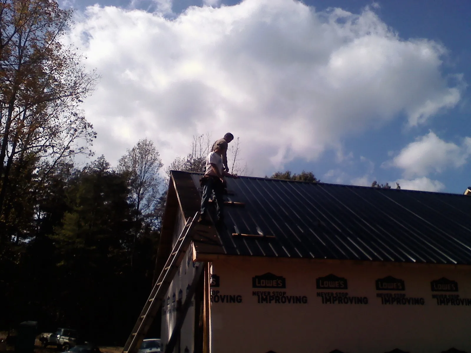 Roofer fastening dark metal panels high against a cloudy sky, from a Roof Inspection job in Napavine