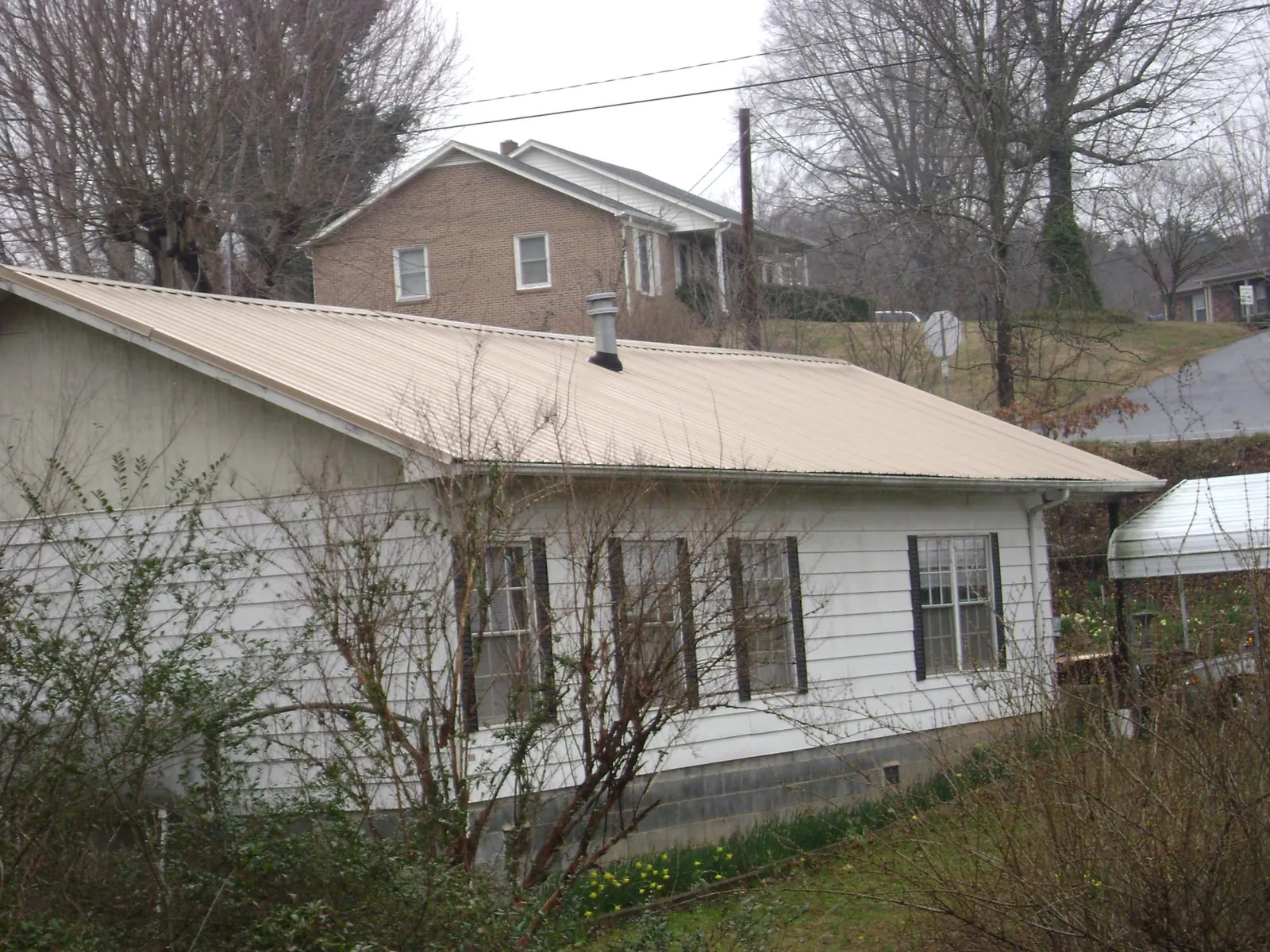 Tan metal roof on a white sided house set into a hillside — Commercial Roofing by Roofing Brothers in Napavine