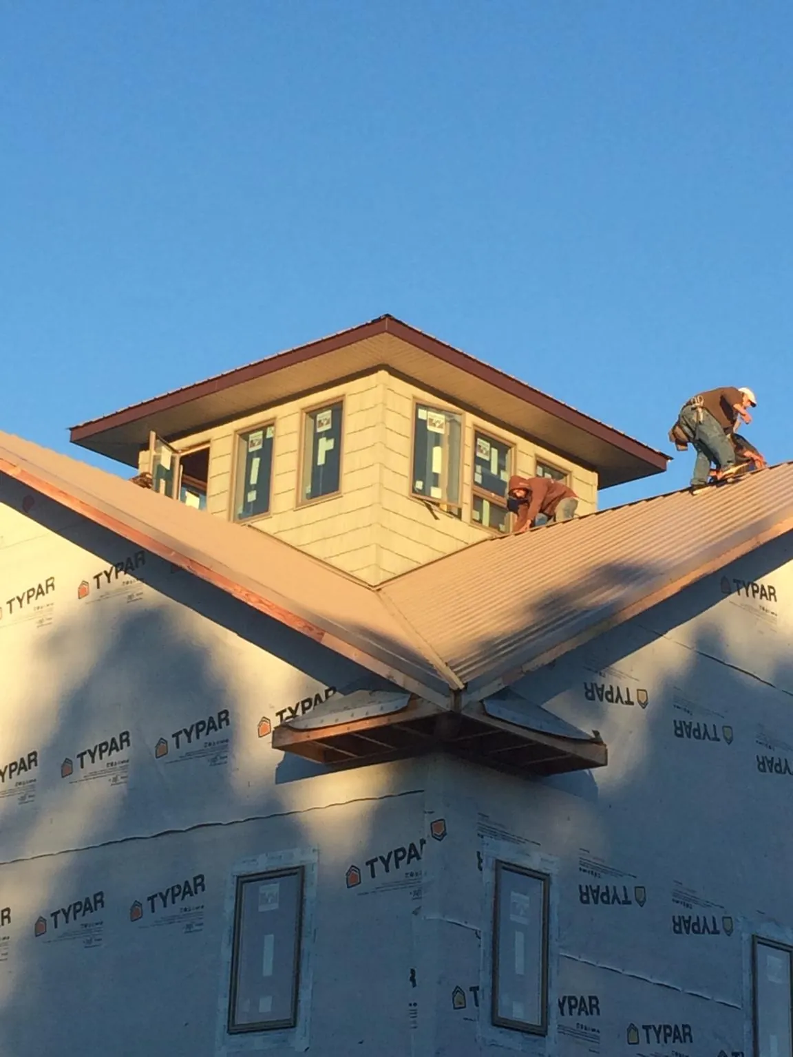 Roofers working around a rooftop cupola on a new metal roof at sunset in Napavine